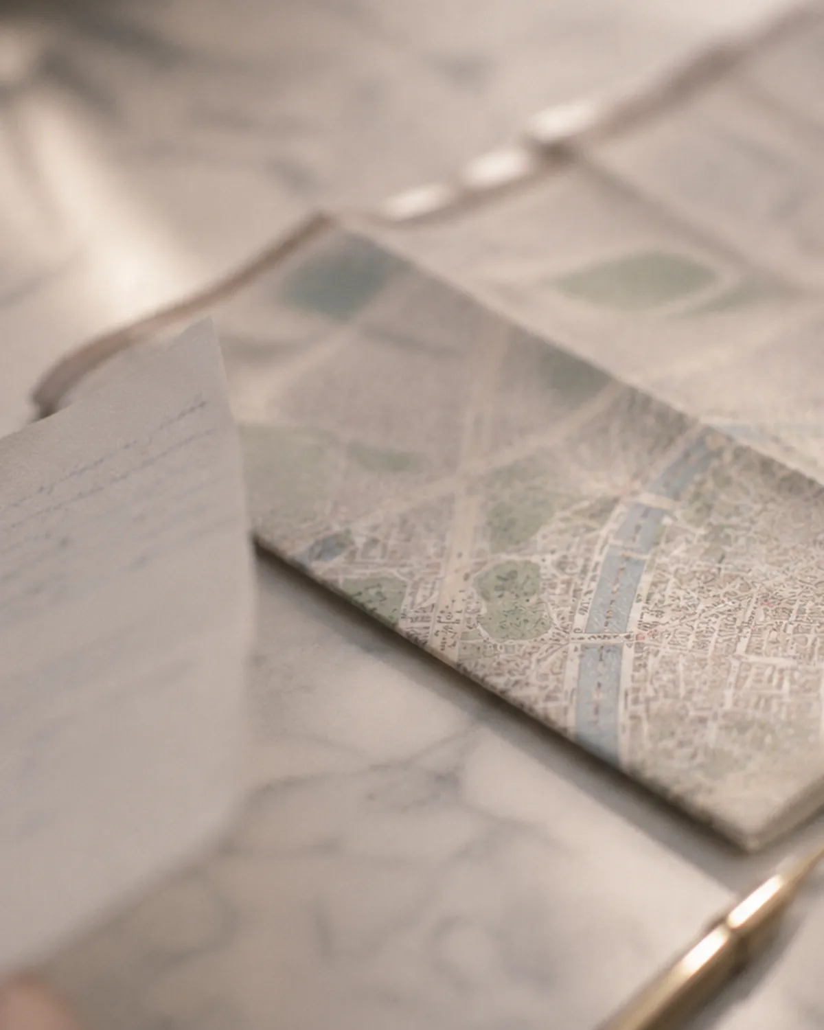 A hand holding a handwritten note beside a folded vintage map of Paris on a marble table — the unclear legal picture couples face from abroad.